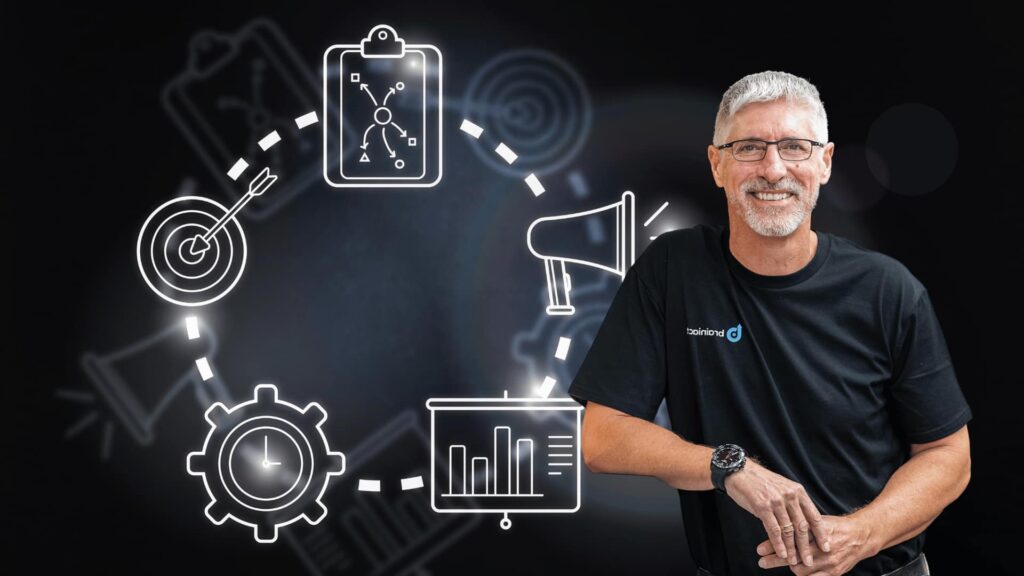 A smiling man in a black shirt stands beside a circular flowchart of glowing business icons on a dark background.