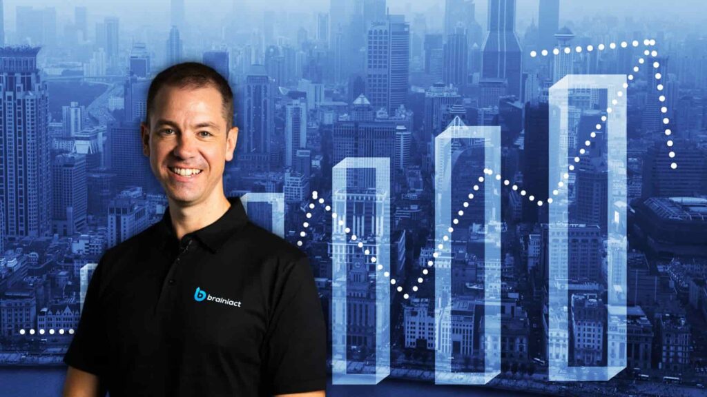 A man stands smiling in front of a city skyline backdrop. Behind him, there are upward-trending bar and dotted line charts, representing business growth and success.