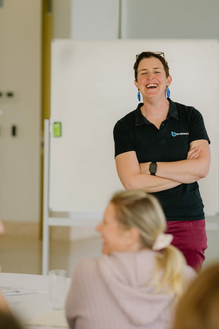 woman laughs in front of a callroom with a whiteboard behind her