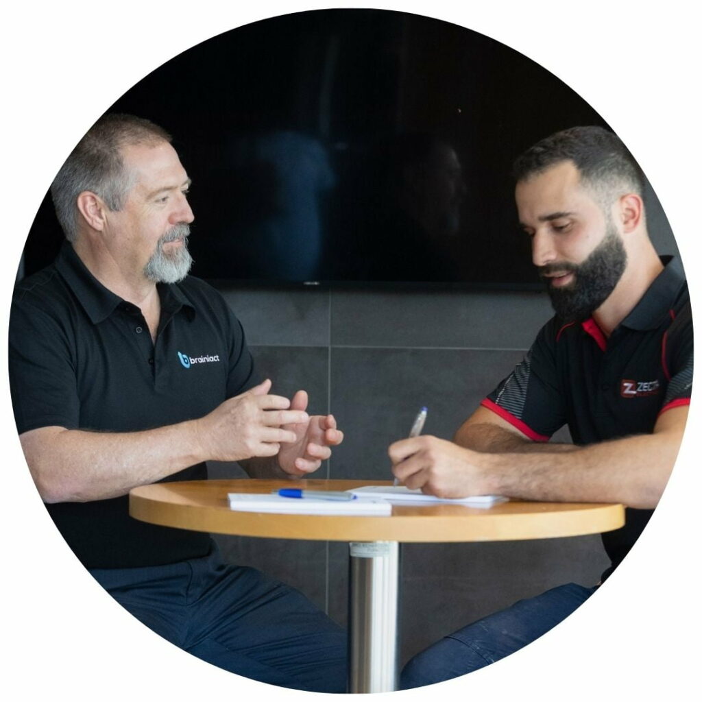 A coach sits at a desk with their client, discussing