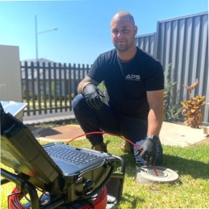 man kneels by plumbing equipment in a yard